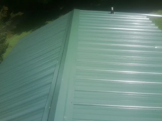 New green metal panels meeting at the ridge of a roof — Flat Roof Repair work by our crew in Sturgis