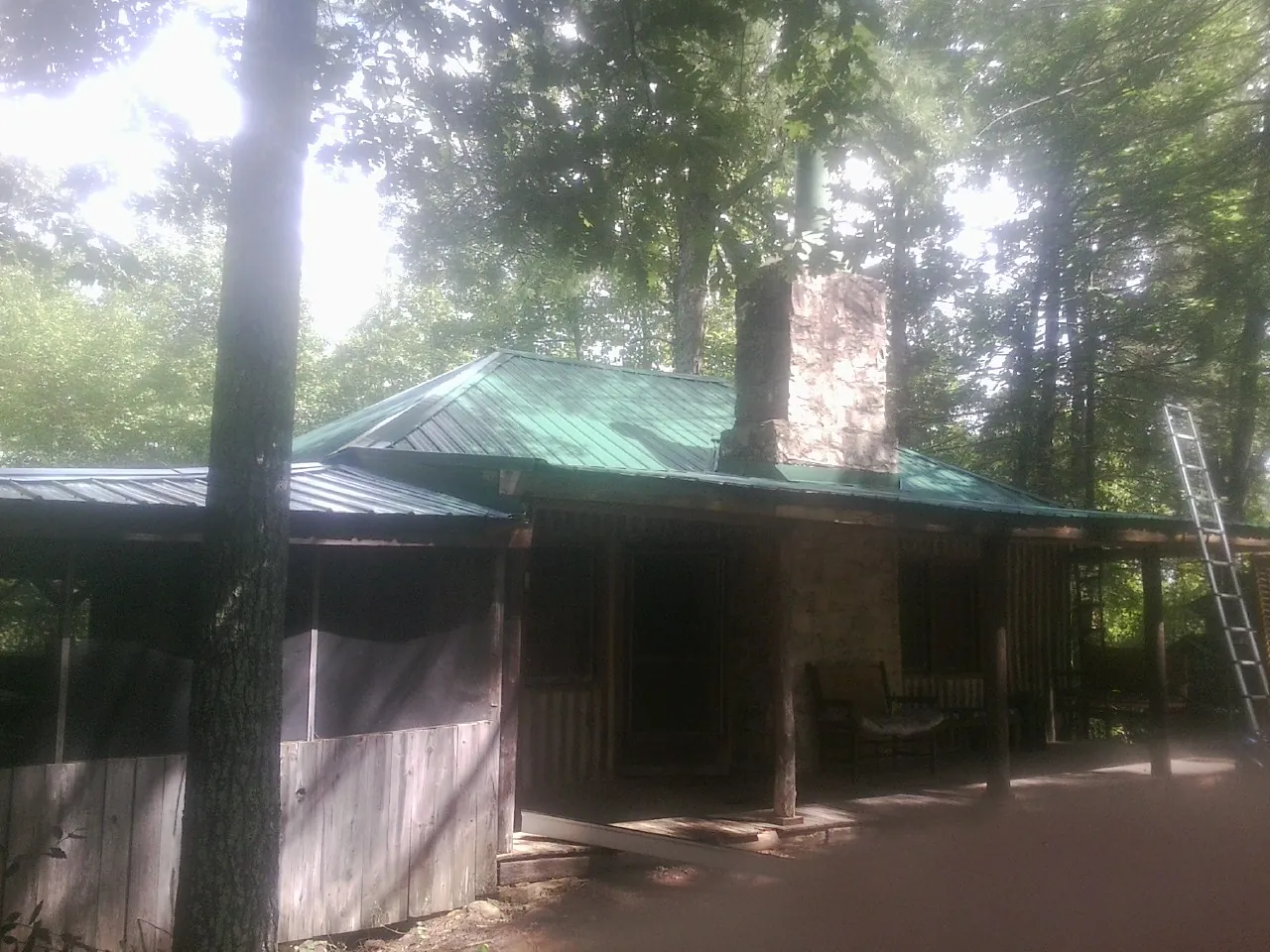 Green metal roof and stone chimney above a log cabin porch in Sturgis