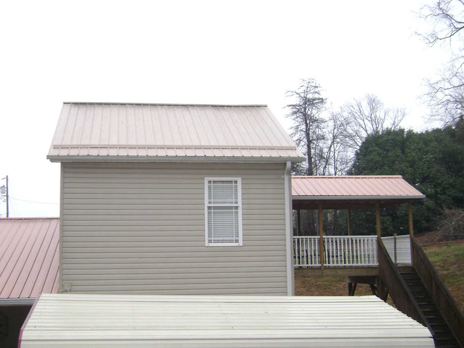 Tan metal roofs on a two story addition and attached porch, from a Roof Replacement job in Sturgis