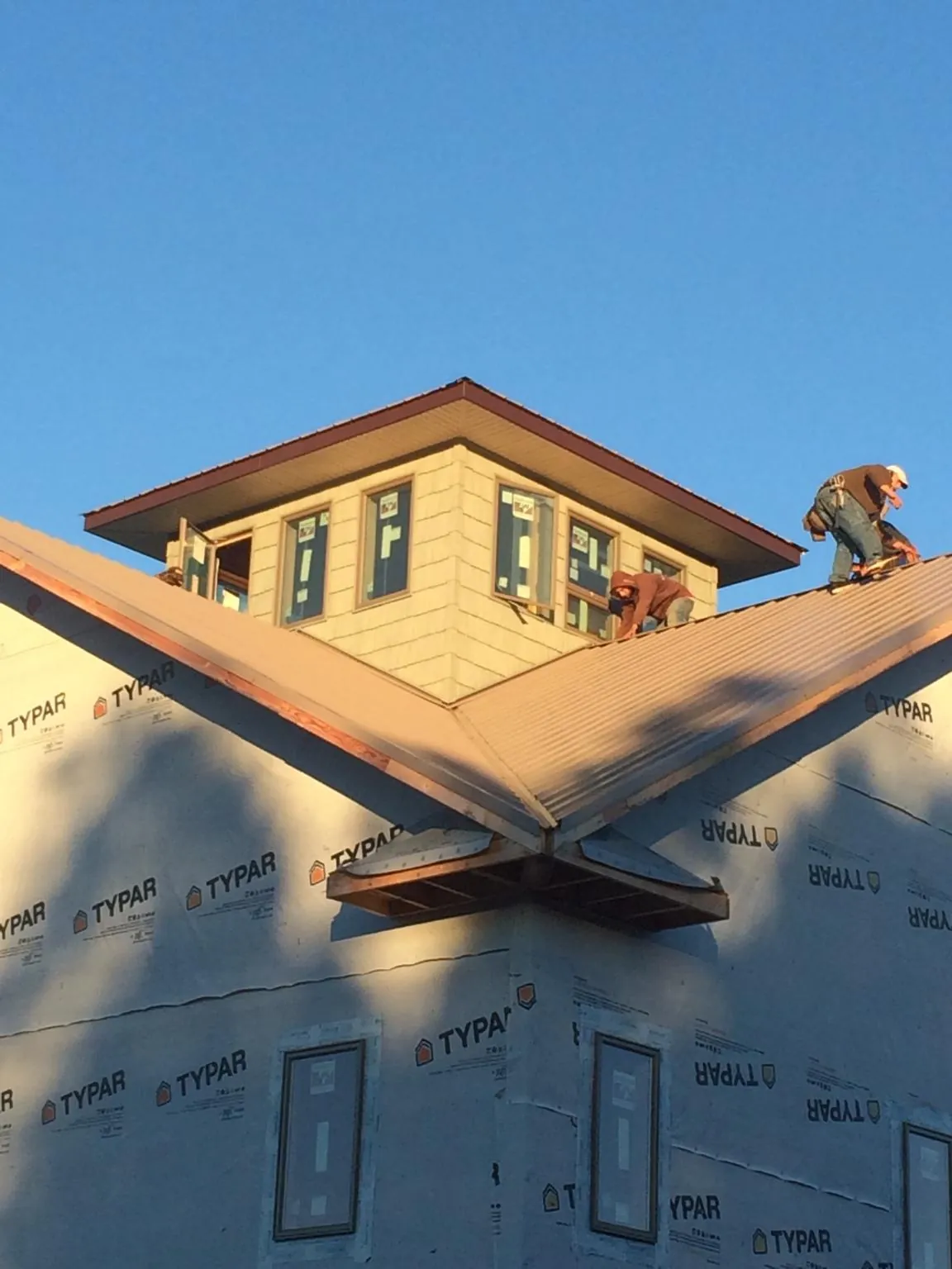 Roofers working around a rooftop cupola on a new metal roof at sunset — Roof Waterproofing in Sturgis by Roofing Brothers